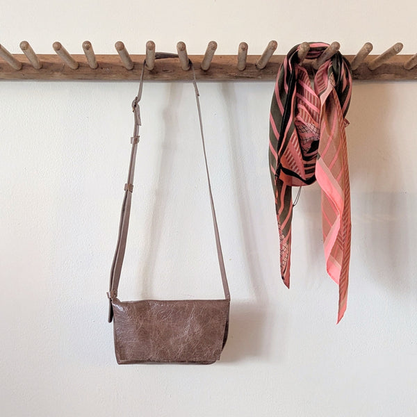 Stitch & Tickle mini messenger bag in Chai and pink scarf hanging on a wooden rack against a white wall.