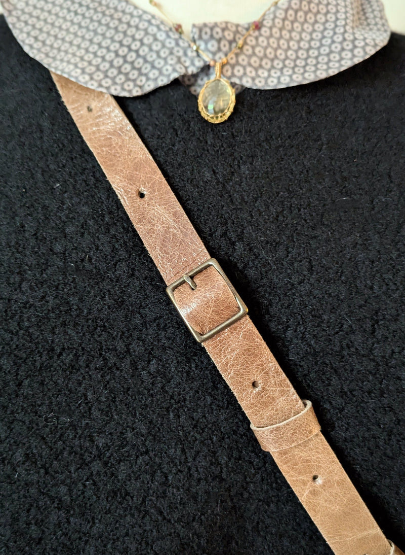Close-up of a brown leather strap with a buckle on a textured black background