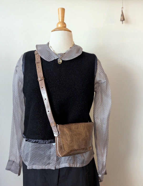 Mannequin wearing a black vest, patterned shirt, and carrying a Stitch & Tickle mini messenger bag in Chai  against a plain background.