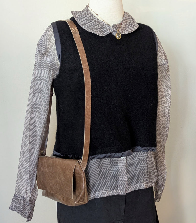 Mannequin wearing a black vest over a patterned shirt with a Stitch & Tickle mini messenger bag in Chai on a white background