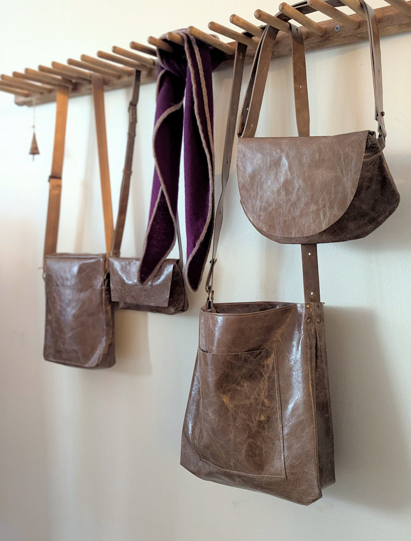 Brown leather bags hanging on a wooden rack against a white wall.