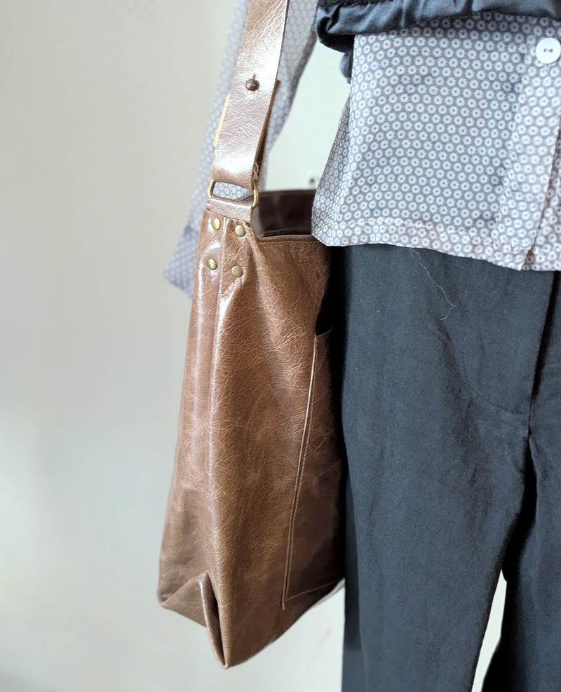 Stitch and Tickle Everyday Carryall bag in Chai  with gold studs held by a person wearing a patterned shirt and dark pants.