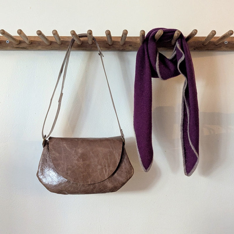Stitch and Tickle Passito bag in Chai  and purple scarf hanging on a wooden rack against a white wall.
