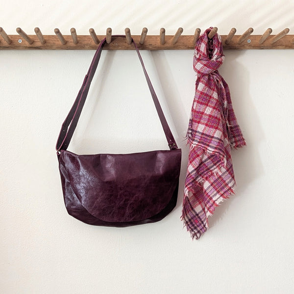Stitch and Tickle Short Passy Bag in Wine and plaid scarf hanging on a wooden rack against a white wall.