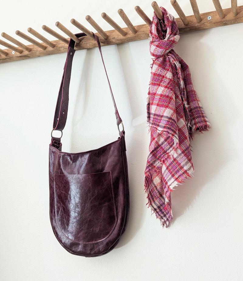 Stitch and Tickle Luna Bag in Wine  and plaid scarf hanging on a wooden rack against a white wall.