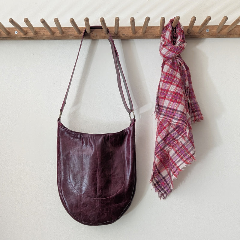 Back of a Stitch and Tickle Luna Bag in Wine  plaid scarf hanging on a wooden rack against a white wall.