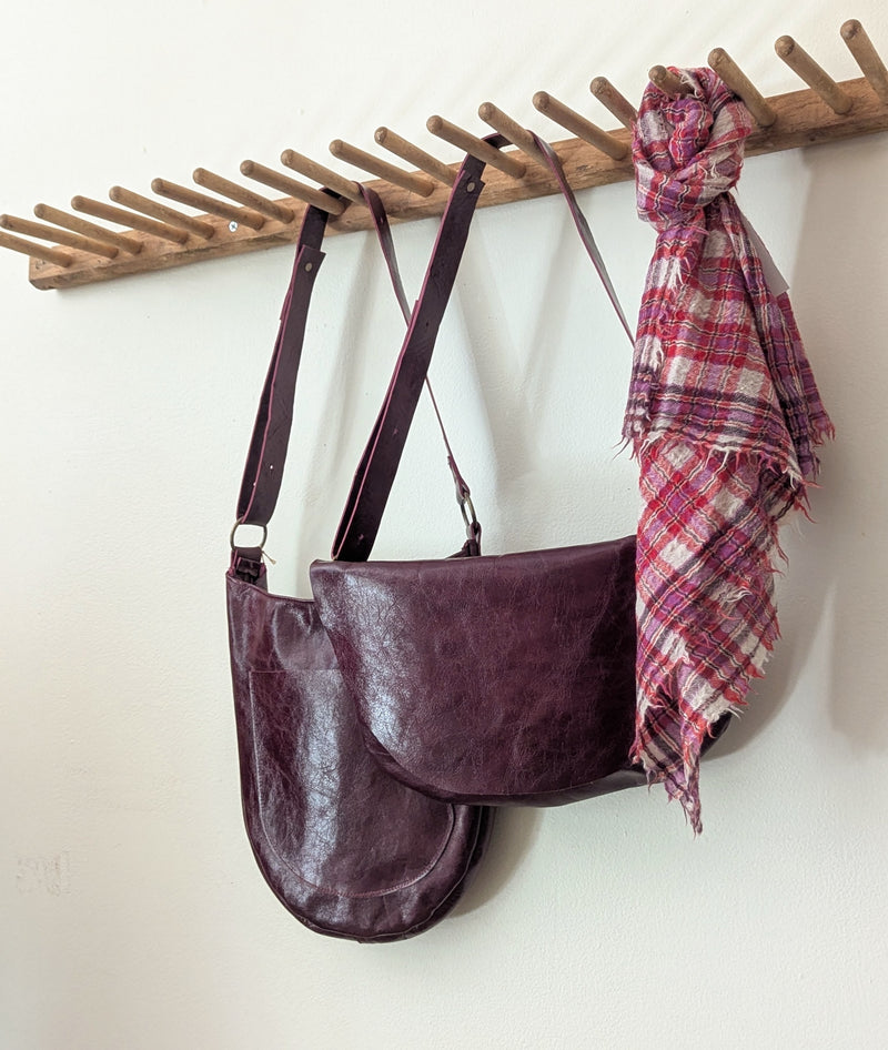 Stitch and Tickle Short Passy Bag in Wine  and plaid scarf hanging on a wooden rack against a white wall.