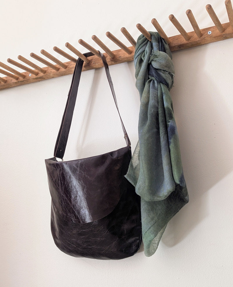 Stitch and Tickle Passy Bag in Espresso  and green cashmere Oats & Rice scarf hanging on a wooden rack against a white wall.
