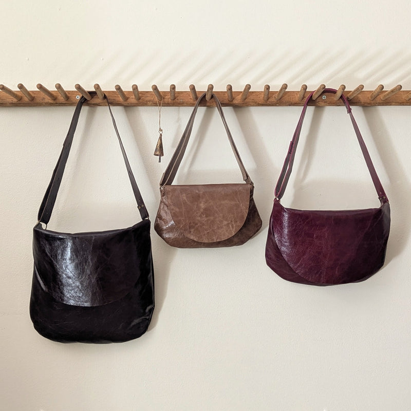 Three leather Stitch & TIckle Passy and Passito handbags hanging on a wooden rod against a white wall.
