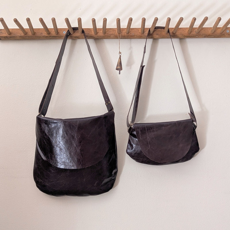 Two stitch and tickle handbags hanging on a wooden rack against a white wall.
