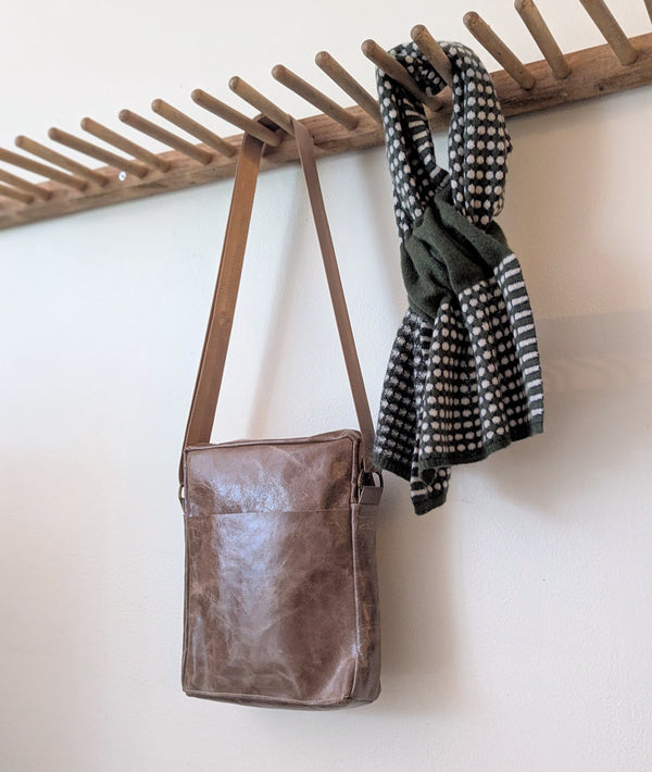 Stitch & Tickle Bourvil Bag in Chai  and green scarf hanging on a wooden rack against a white wall.