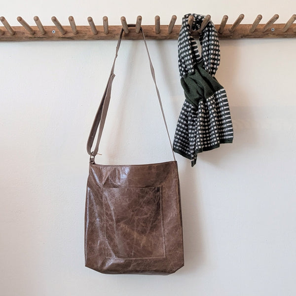 Stitch and Tickle Everyday Carryall bag in Chai hanging on a wooden rack against a white wall.