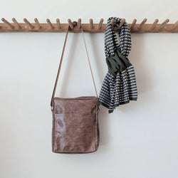Stitch & Tickle Bourvil Bag in Chai and a green and white checkered scarf hanging on a wooden rack against a white wall.