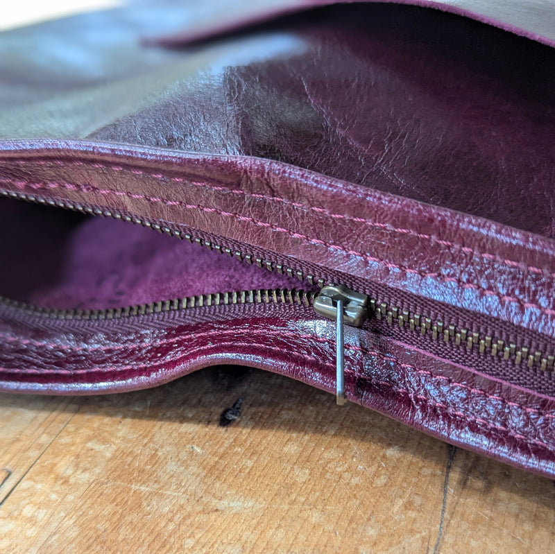 Close-up of a zipper from the Stitch and Tickle Luna Bag in Wine on a wooden surface