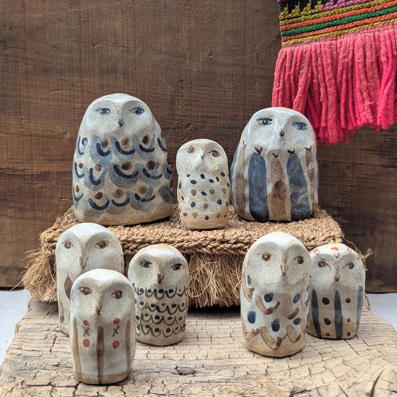 Set of ceramic owl figurines on a wooden surface with a colorful fabric background.
