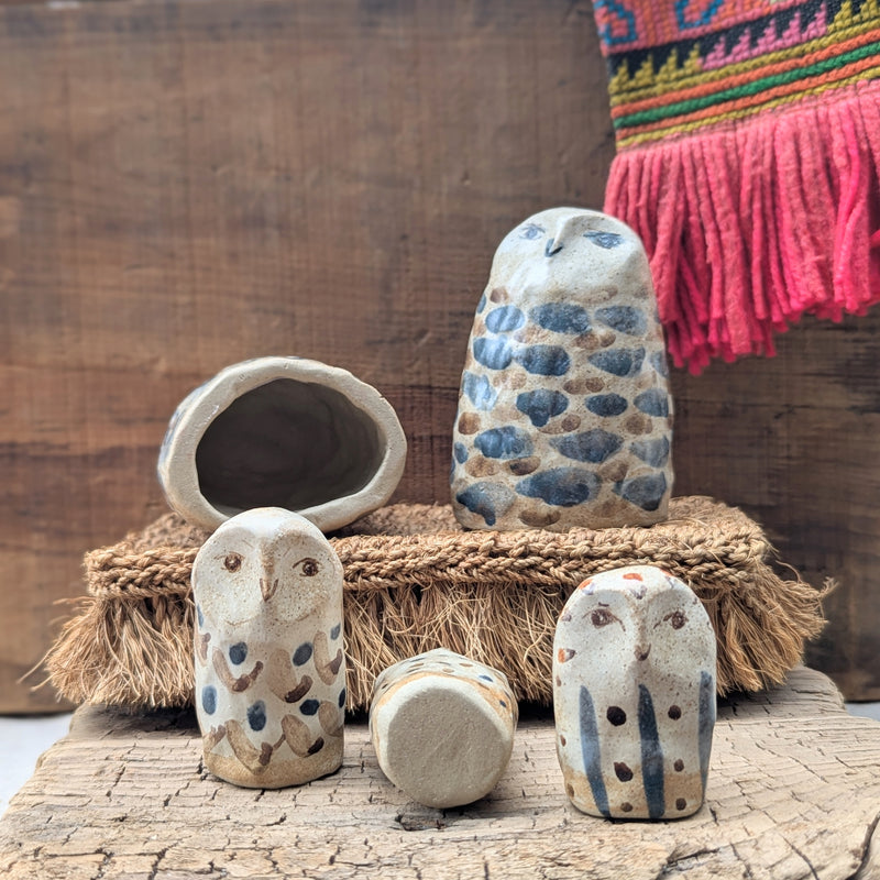 Set of ceramic owl figurines on a wooden surface with a colorful fabric in the background.