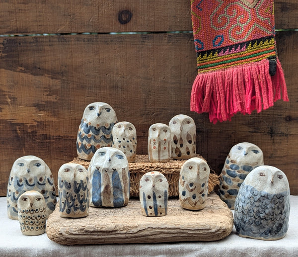 Collection of ceramic owl figurines on a wooden base with a colorful fabric in the background.