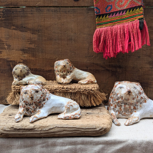 Four ceramic lion figurines on a wooden surface with a colorful woven scarf in the background.
