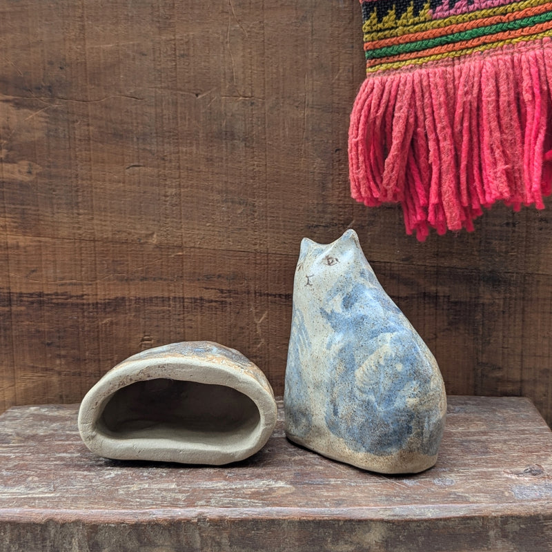 Two stone cat sculptures on a wooden surface with a colorful woven fabric in the background.