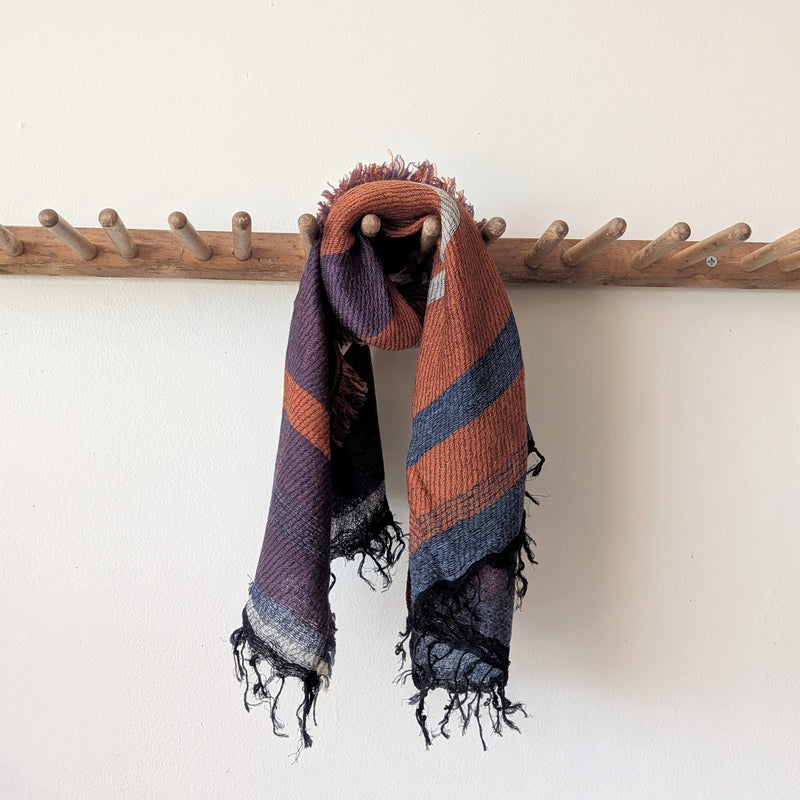 Multicolored striped scarf draped over a wooden coat rack against a white wall.