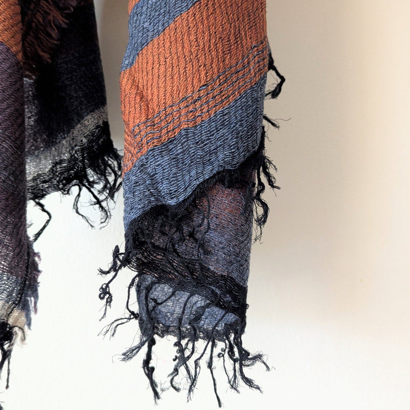 Textured scarf with fringes in orange, blue, and black on a neutral background