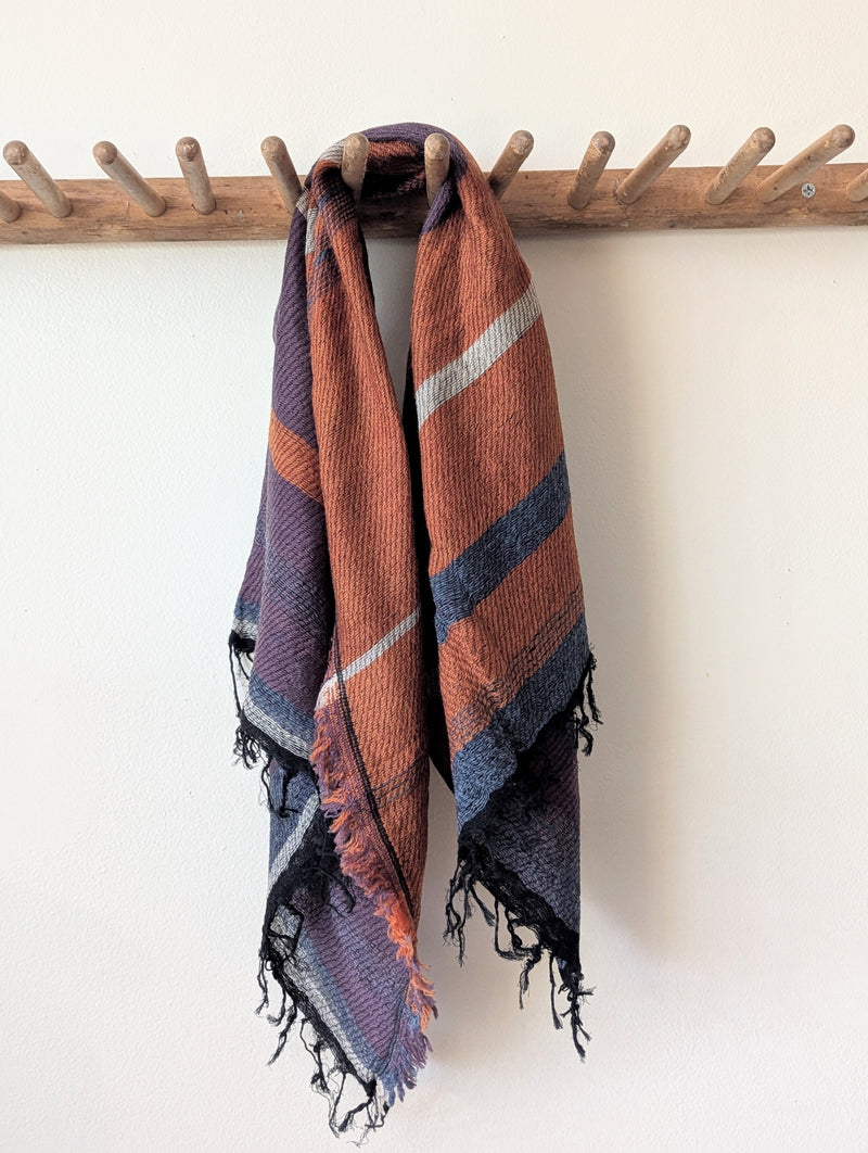 scarf with purple, orange, and blue colors draped over a wooden coat rack on a white background.