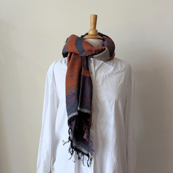 Mannequin wearing a white shirt with a multi colored stripe scarf draped over it against a plain background