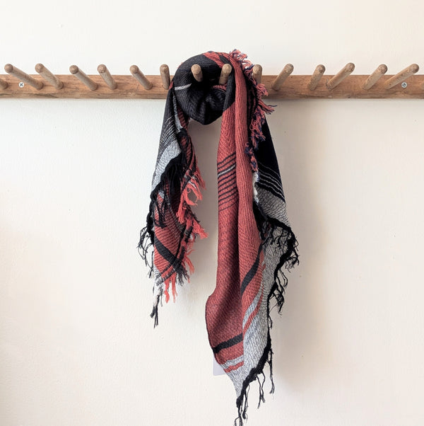 Black and red patterned scarf draped over a wooden coat rack on a white wall.