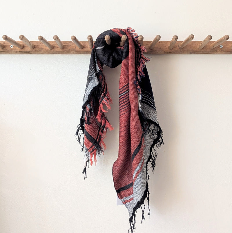 Black and red patterned scarf draped over a wooden coat rack on a white wall.