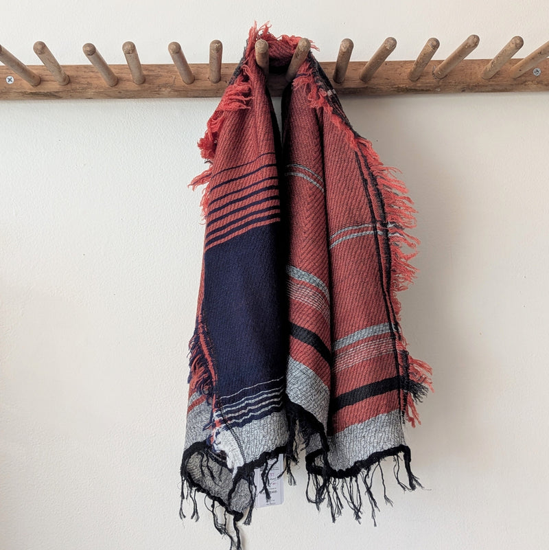 Patterned scarf hanging on a wooden rack against a white wall.