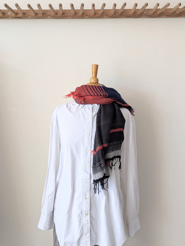 Mannequin wearing a white shirt with a colorful scarf draped over it against a plain wall.