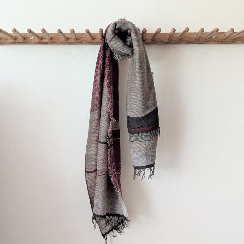 Plaid scarf with fringe hanging on a wooden rack against a white wall