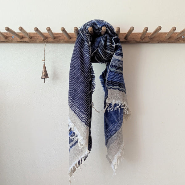 Blue and white patterned scarf hanging on a wooden rack against a white wall.