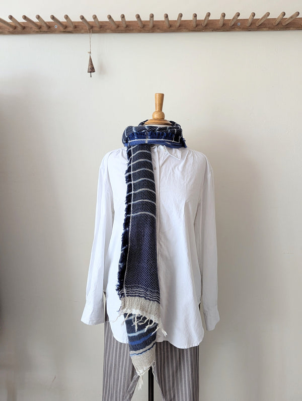 White shirt with a blue patterned scarf draped over it on a wooden mannequin against a white background.