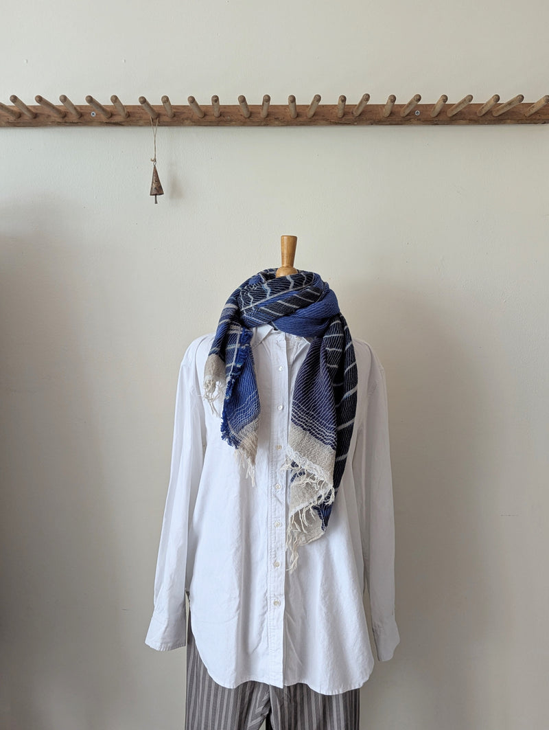 White shirt with a blue patterned scarf on a wooden mannequin against a plain wall.