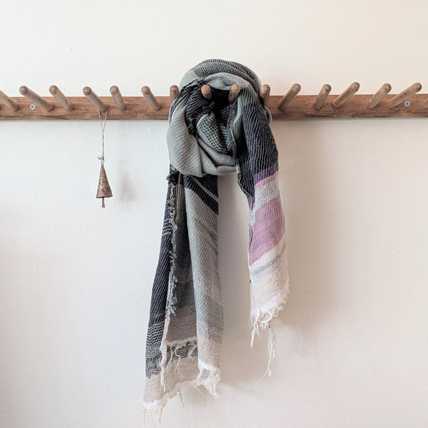 Textured scarf hanging on a wooden coat rack against a white wall.