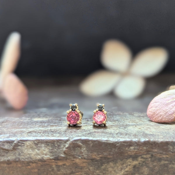 Gold earrings with pink gemstones  and black diamonds on a wood surface