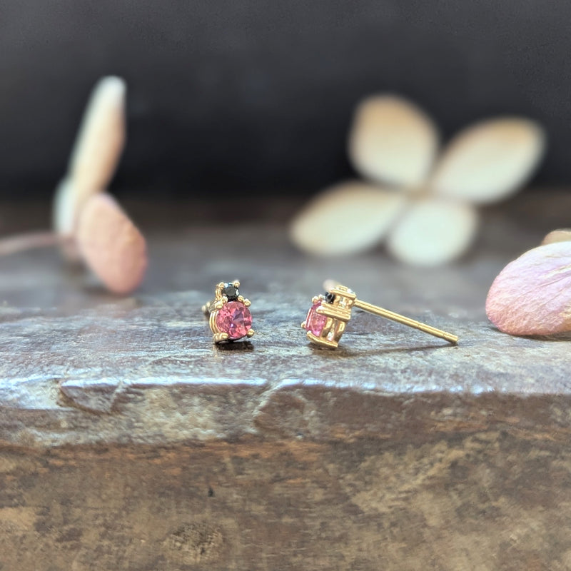 Gold earrings with pink gemstones  and black diamonds on a wood surface