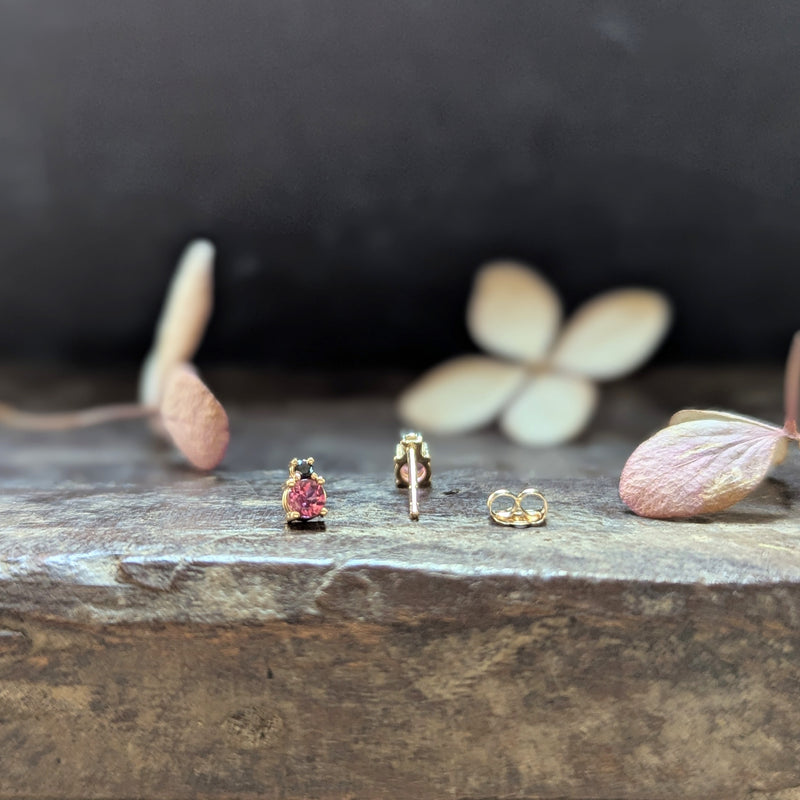 Gold earrings with pink gemstones  and black diamonds on a wood surface