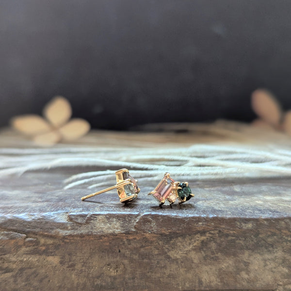 Pair of gold stud earrings with gemstones on a textured surface