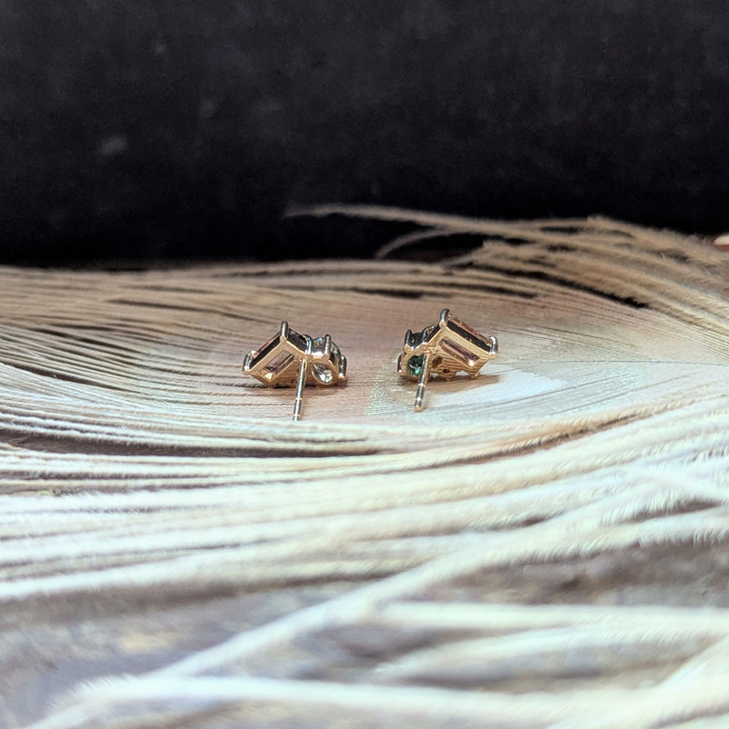 Gold stud earrings with green and gemstones on a textured surface