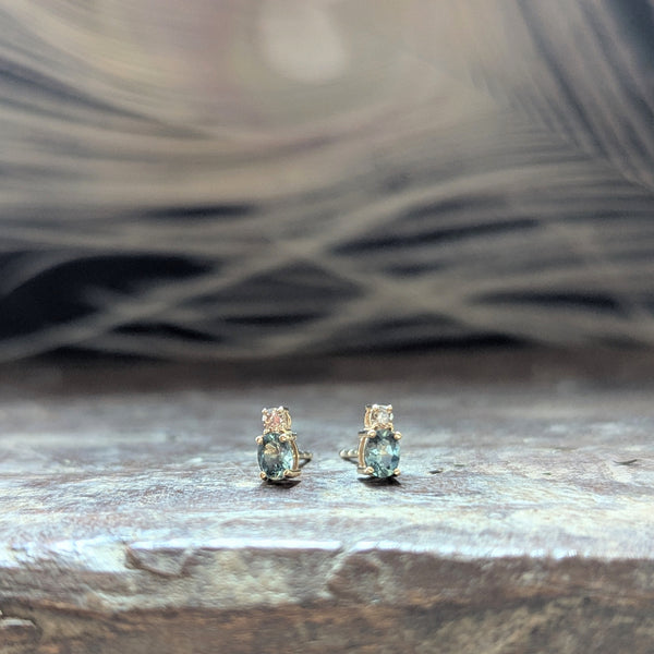 Pair of gold earrings with blue sapphire gemstones and a diamond on a wooden surface