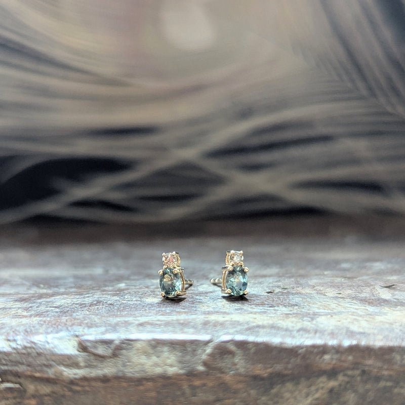 Pair of gold earrings with blue sapphire gemstones and a diamond on a wooden surface