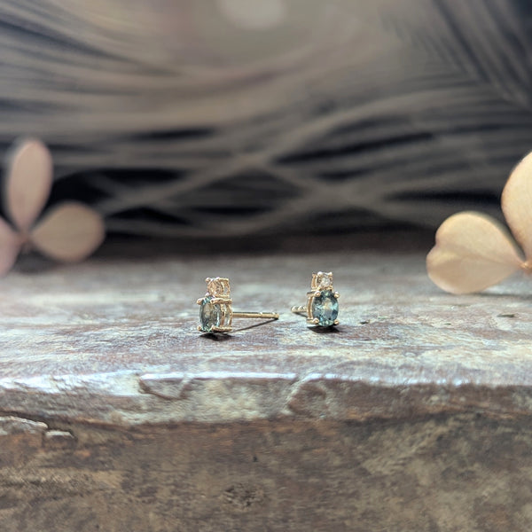 Pair of gold earrings with blue sapphire gemstones and a diamond on a wooden surface