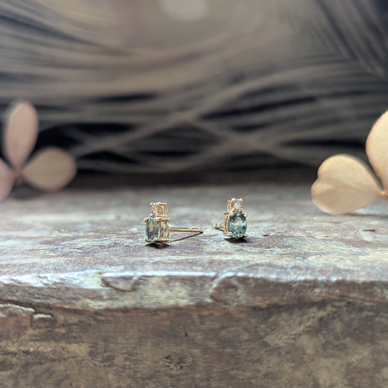 Pair of gold earrings with blue sapphire gemstones and a diamond on a wooden surface