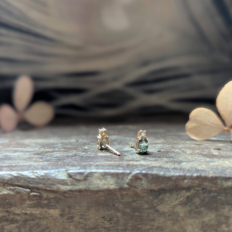 Pair of gold earrings with blue sapphire gemstones and a diamond on a wooden surface