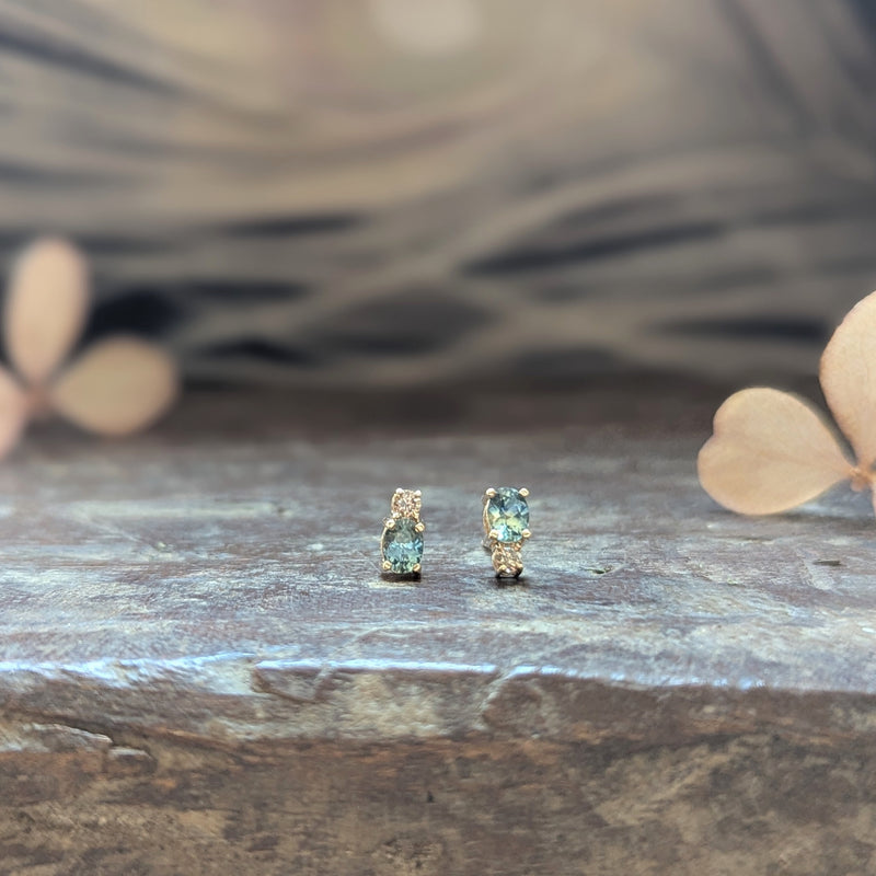 Pair of gold earrings with blue sapphire gemstones and a diamond on a wooden surface