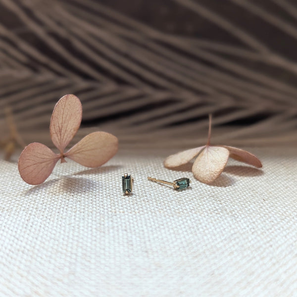 Pair of earrings with Green Tourmaline gemstones on a textured surface with dried leaves.