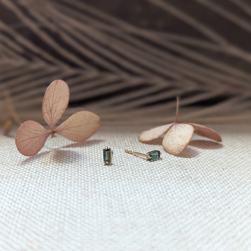 Pair of earrings with Green Tourmaline gemstones on a textured surface with dried leaves.