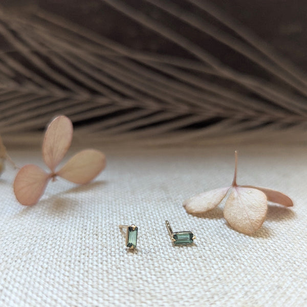 Pair of earrings with Green Tourmaline gemstones on a textured surface with dried leaves.
